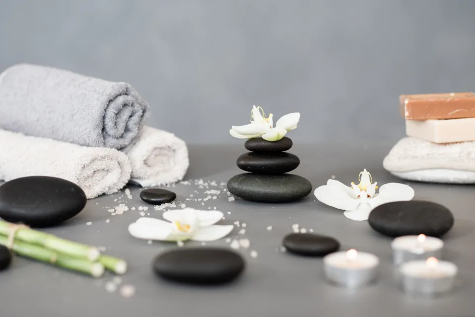 Rolled white towels in pairs beside massage stones, white orchids, and lit candles
